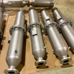 Several large, cylindrical, metallic industrial components with flanges are arranged on a cardboard-covered floor in a workshop or factory setting.